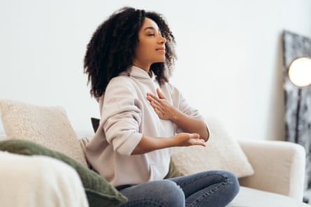 A young woman practicing breathing exercises sitting on sofa at home
