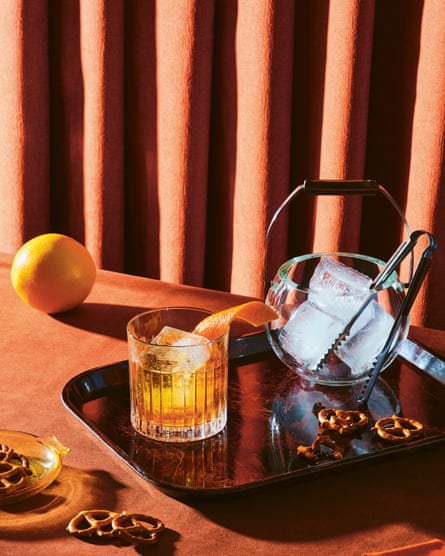 An old-fashioned cocktail on a tray, next to a bowl of ice.  The tray is decorated with pretzels.