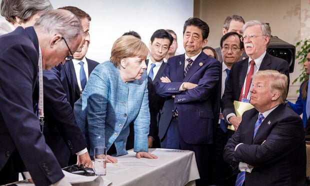 Donald Trump talking with Angela Merkel and surrounded by other G7 leaders during a meeting of the G7 Summit in La Malbaie, Quebec, Canada.