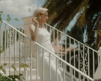 Actress Valeria Bruni Tedeschi in a white dress leans on a metal staircase, smoking, in a film still from The Spiral