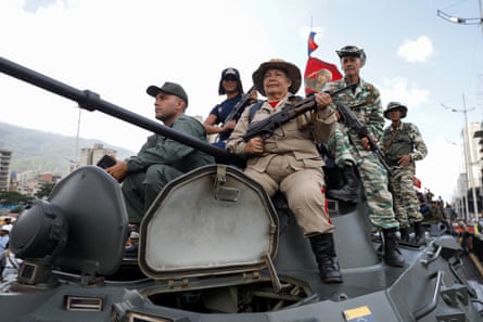 they hold a Venezuelan flag and some wear camouflage. The tank is being driven down a street.