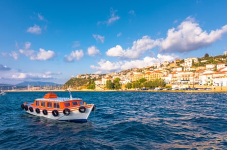 A small boat in blue sea and in background a picturesque Greek coastal town
