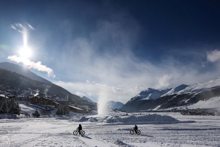 Cyclists ride on a snow-covered field as artificial snow rises from a snowmaking cannon in Livigno