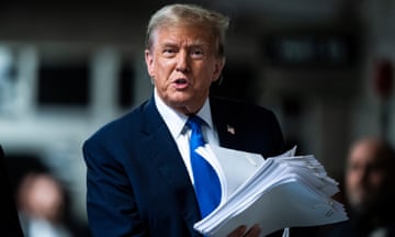 Trump holds print outs of news stories as he speaks to reporters at the end of the third day of his trial in New York. 