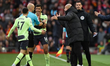 The Manchester City manager, Pep Guardiola, and his players surround referee Anthony Taylor as he goes to the screen to look at a VAR review.