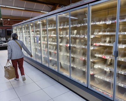 A woman walks past empty refrigerators at an Intermarché supermarket