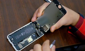 A battery is exposed as a man tries to repair an iPhone in a repair store in New York.
