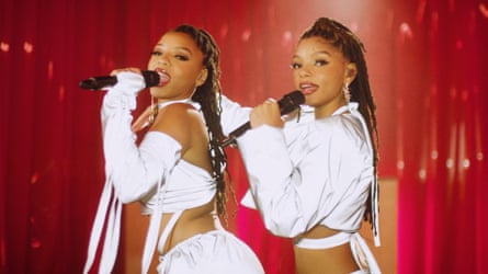 Wearing matching cropped white tops, they dance and sing on stage, each holding a microphone