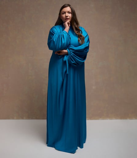 Hannah Murray wears a floor-length satin dress with puffy sleeves. Her long dark hair is worn down