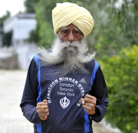 Fauja Singh, fists pumping out on a street, wearing a 'marathon winner' sports top, and with a turban and long grey beard.