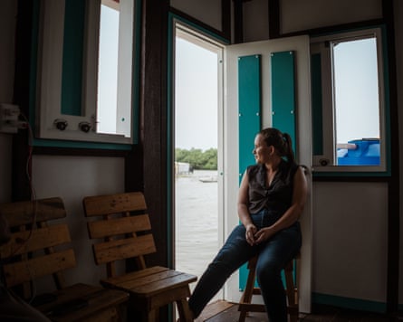 A young woman sits by an open door in a cabin looking out over water