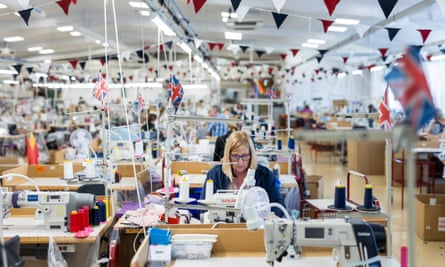 The main garment sewing room at David Nieper in Alfreton is decorated with union flags and bunting, with seamstress Donna Wass working at a machine.