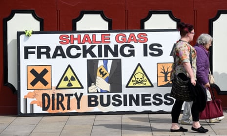 People walk past an anti-fracking banner