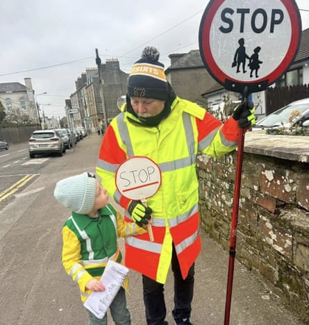 Lollipop man with a young boy who carries a homemade “Stop” lollipop sign