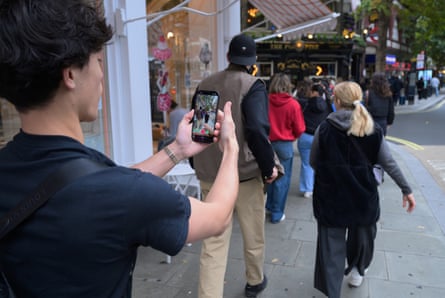 Roh points his phone camera at a couple walking on the pavement ahead of him.