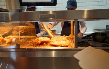 A man puts fried fish under a heat lamp in a restaurant kitchen