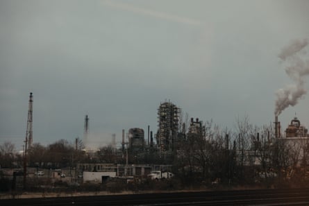 An oil refinery billows smoke into a cloudy sky.
