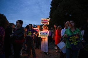 A woman holds two signs illuminated with fairy lights surrounded by other protesters at dusk