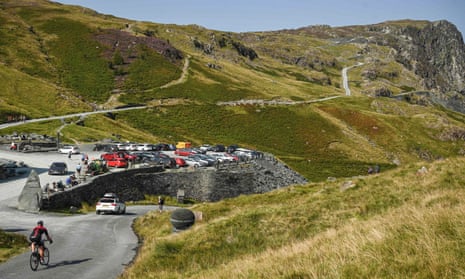 A cyclist passes the busy car park at the slate mine on Honister Pass in the Lake District.