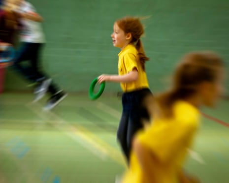 Children in yellow shirts run indoors with motion blur, one holding a green ring