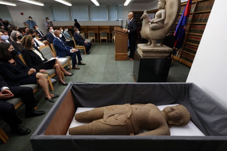 man speaks at podium to listening audience, with a statue in a box in the foreground