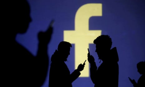 Silhouettes of mobile users are seen next to a screen projection of Facebook logo