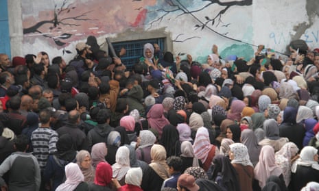 A large crowd of people wait outside a building painted with a mural of tree branches