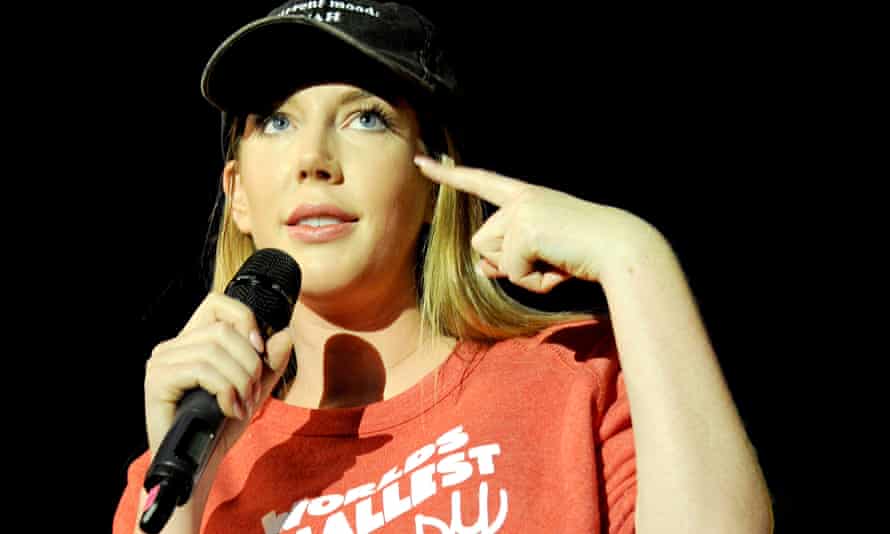 Katherine Ryan performing connected stage, holding a mic and wearing a cap