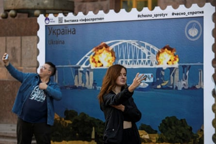 People in Kyiv take selfies in front of an artwork depicting the Kerch bridge on fire.