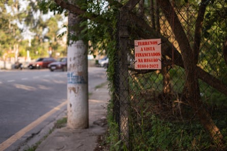 A wooded sign on a tree by a roadside advertises land for sale in the region with a phone number.