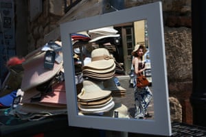 A tourists wearing a hats is reflected in a mirror as she strolls in the city centre
