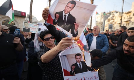 Woman surrounded by other people burning picture of Emmanuel Macron
