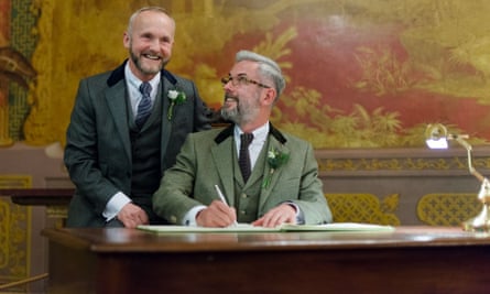 Nick Allard stands as Andrew Wale, seated at a desk, signs the wedding document
