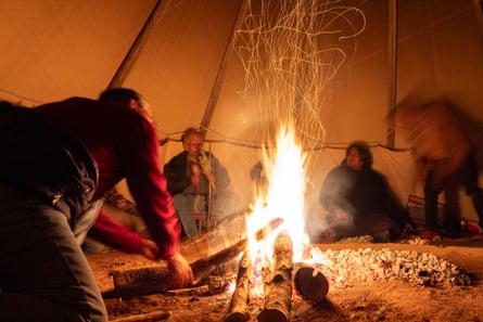 Man putting log on fire as people sit around it
