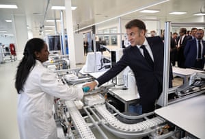 Emmanuel Macron shakes hands with a woman in a white coat working on a production line