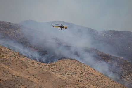 helicopter in air as smoke rises on dry hillsides