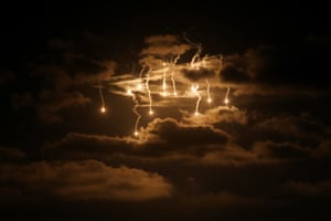 Flares light up the night sky, illuminating the clouds