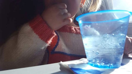 A young girl on a flight drinks from a blue cup with a straw on a sunlit tray table