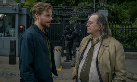 Jack Lowden, with a bloodied face, and Gary Oldman stand in the street outside a security gate
