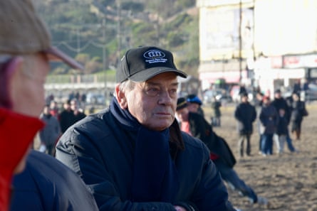 Dickie Bird out in Scarborough wearing a thick jacket and cap and looking away from the camera