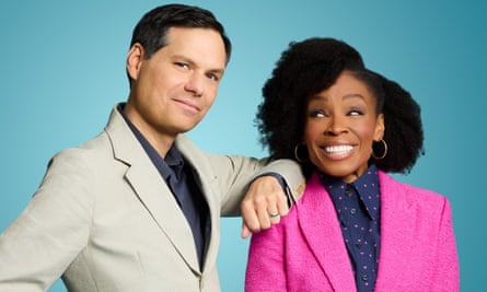 A man wearing a tan suit rests his elbow on the shoulder of a woman next to him, who wears a pink suit
