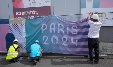 Workers hang a banner that says ‘Paris 2024’ on a metal fence