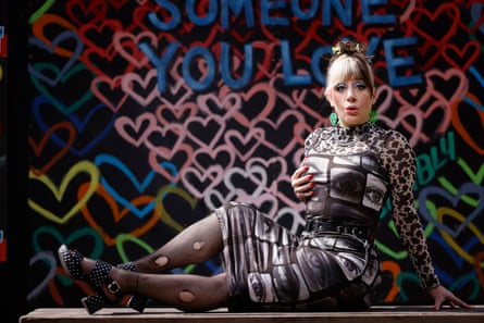 A womn in front of an installation of hearts with the words ‘You Love’ on it. She has blond hair and a tiger print dress