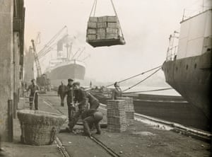 Dockers unloading crates of potatoes into a large basket