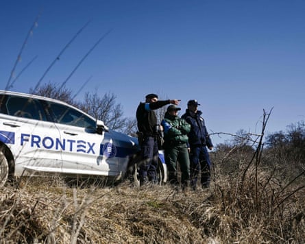 three men stand beside a car which has Frontex written on its side