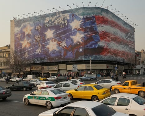 People walk past a billboard displaying the Iranian flag in Tehran