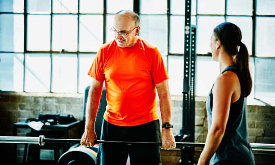 A coach teaches a senior man on the barbells.