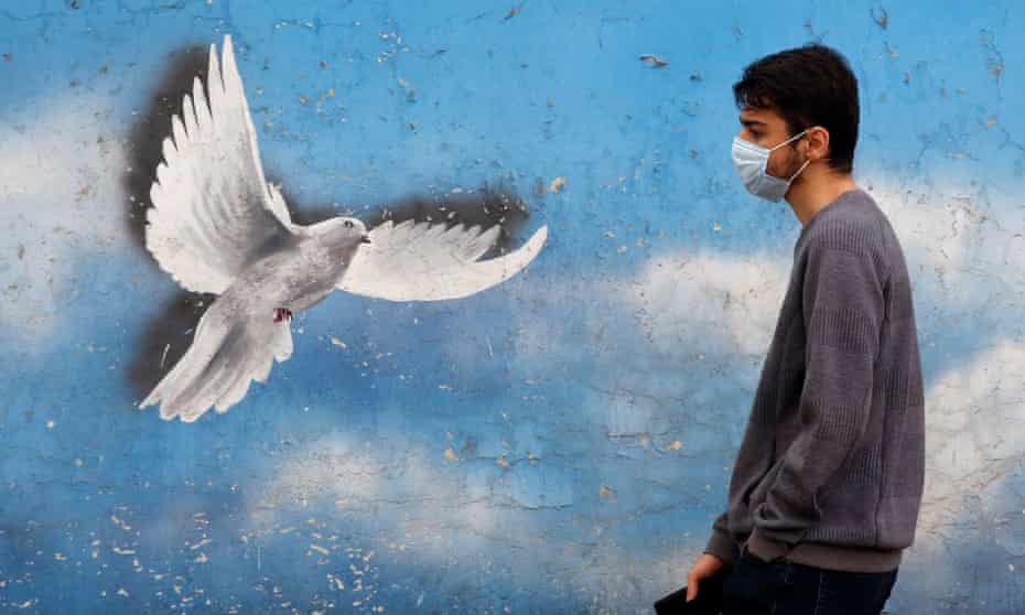 An Iranian wearing a face mask walks past a mural in a street in Tehran