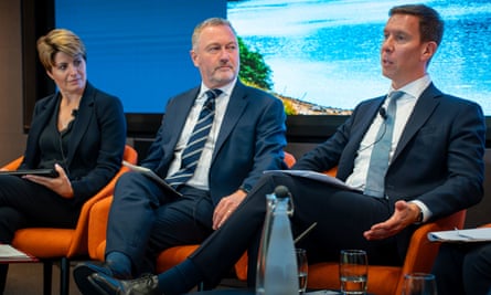 Seated in a row, Emma Hardy and Steve Reed look at Spencer Livermore as he speaks in front of a photo of a lake