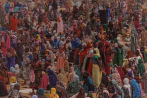 A crowd of people wait for a food distribution point to open at a temporary camp